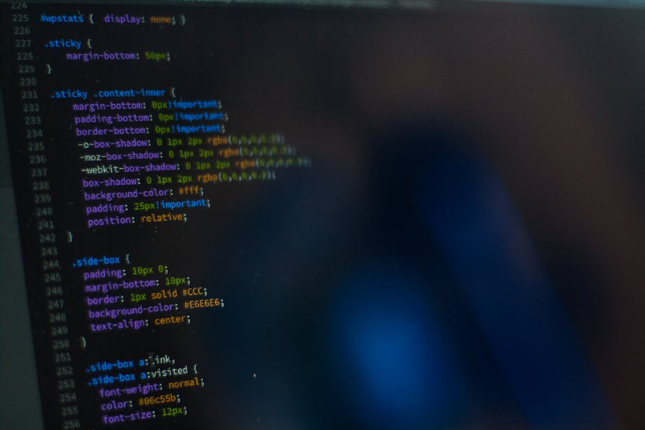 A close-up image of a computer screen displaying lines of colorful code, including CSS and HTML elements. The code features various styles such as margins, borders, text alignment, and background colo